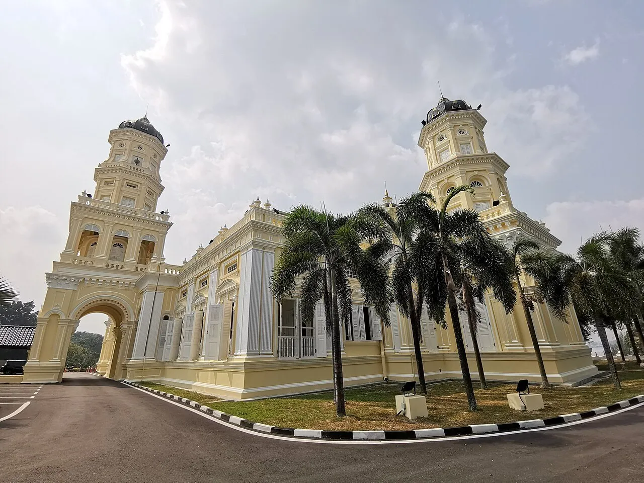 Exterior da Mesquita Sultan Abu Bakar em Johor Bahru, com duas torres claras e palmeiras.