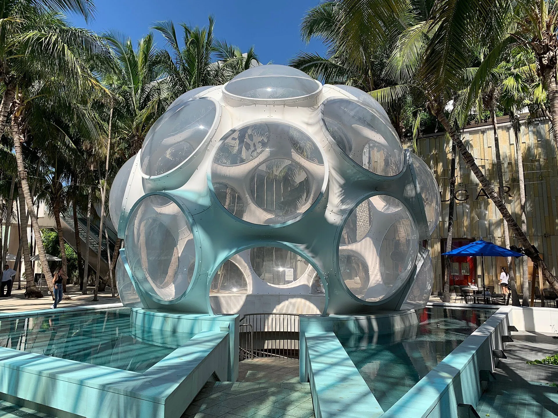 Cúpula branca com aberturas circulares em Palm Court, entre palmeiras e lojas do Miami Design District.