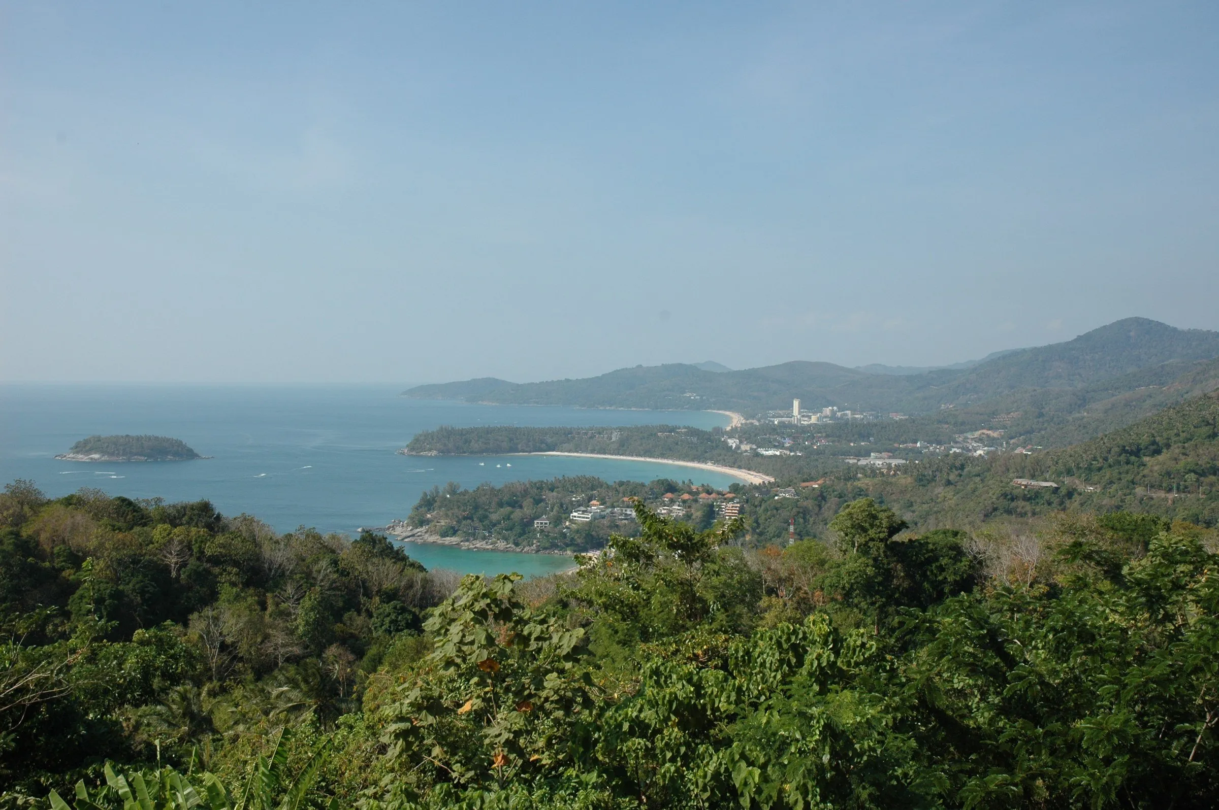Vista de cima das baías de Kata Noi, Kata e Karon, com a ilhota Koh Pu no mar, entre a mata em primeiro plano.