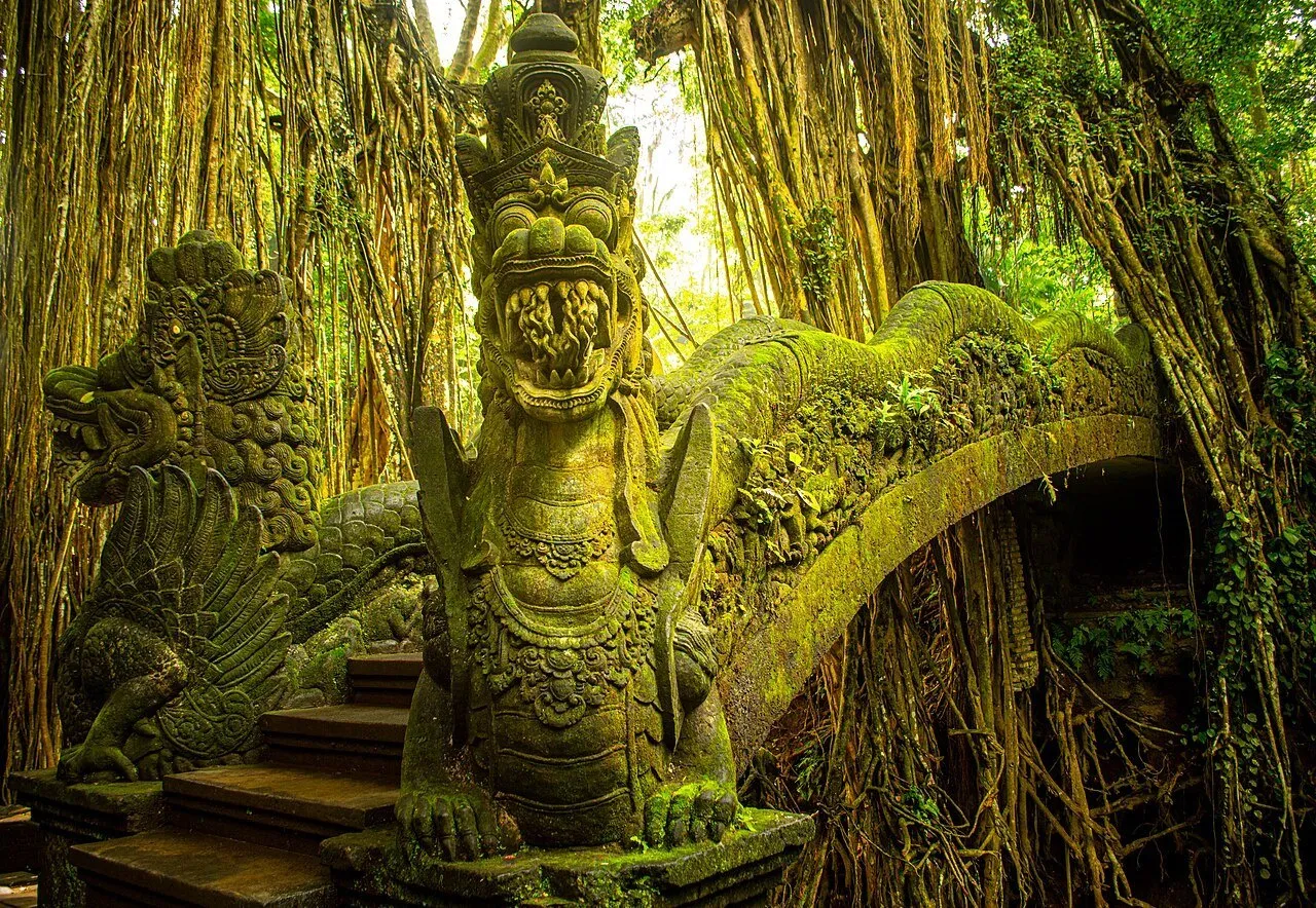 Ponte de pedra com esculturas de dragões e musgo, cercada por raízes pendentes na Monkey Forest de Ubud.