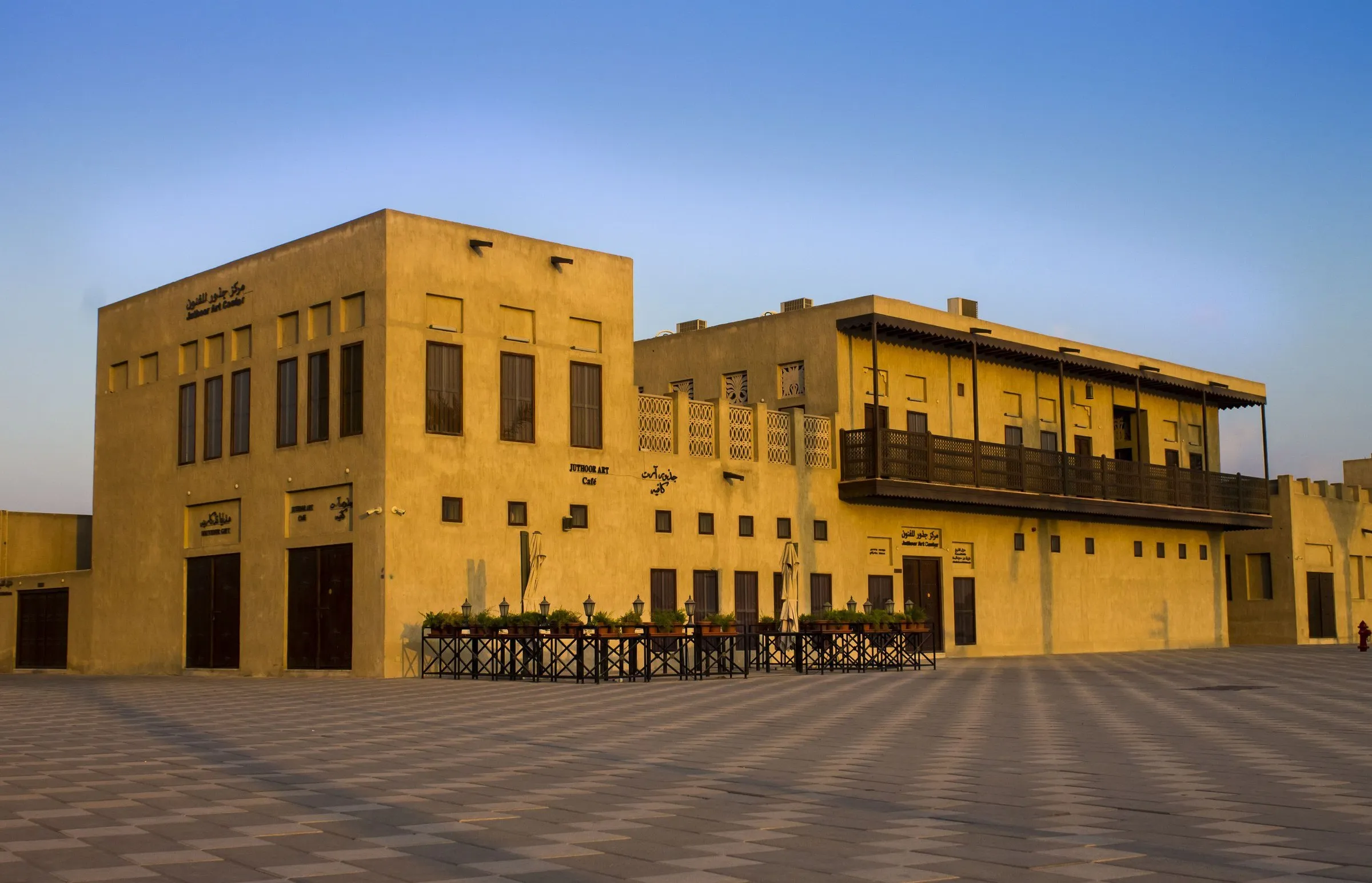 Casas históricas restauradas do bairro de Shindagha, em tom de areia sob a luz dourada do fim da tarde, numa praça vazia.
