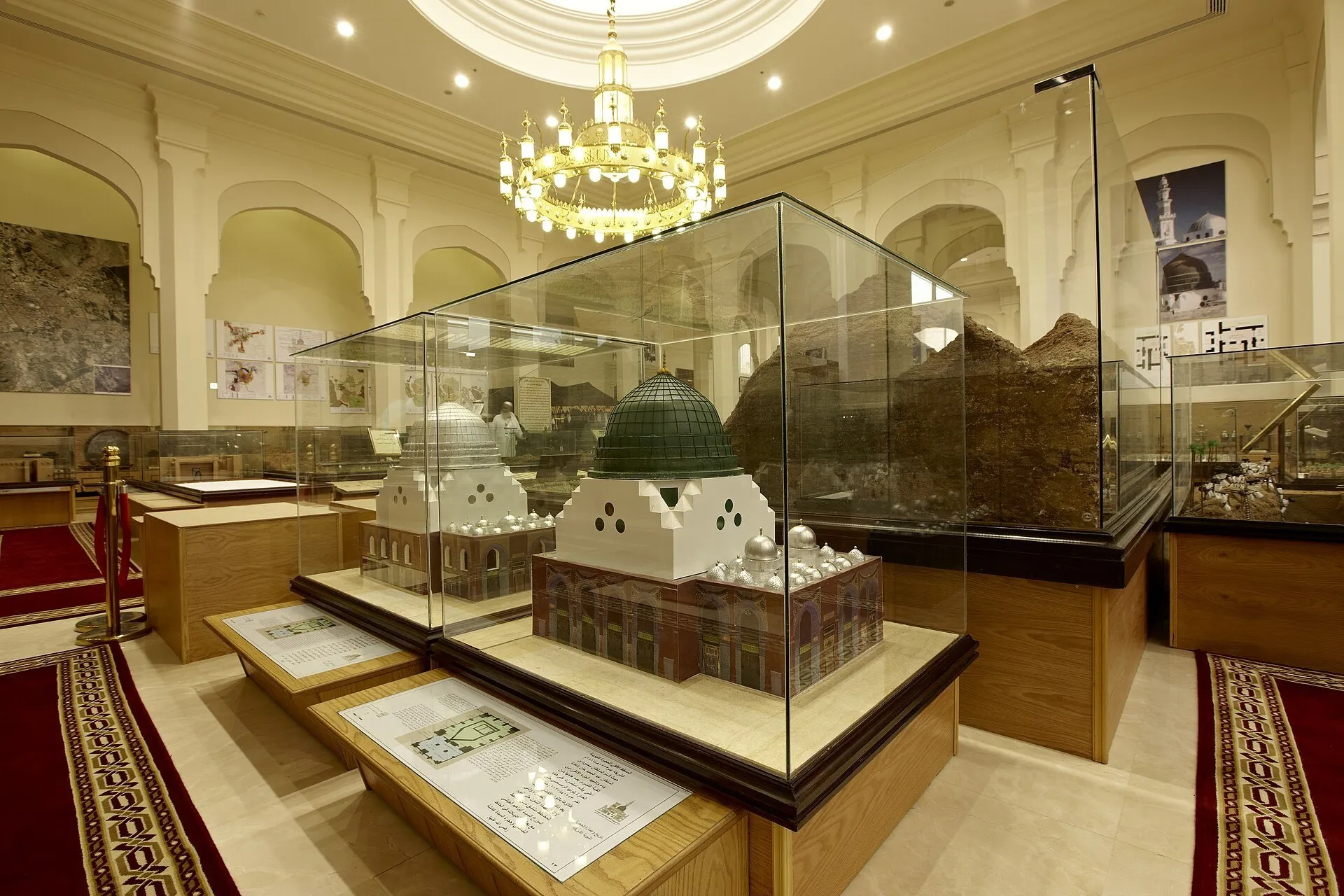 Maquetes de edifícios com cúpulas em vitrines do Museu Dar Al-Madinah, numa sala com lustre.