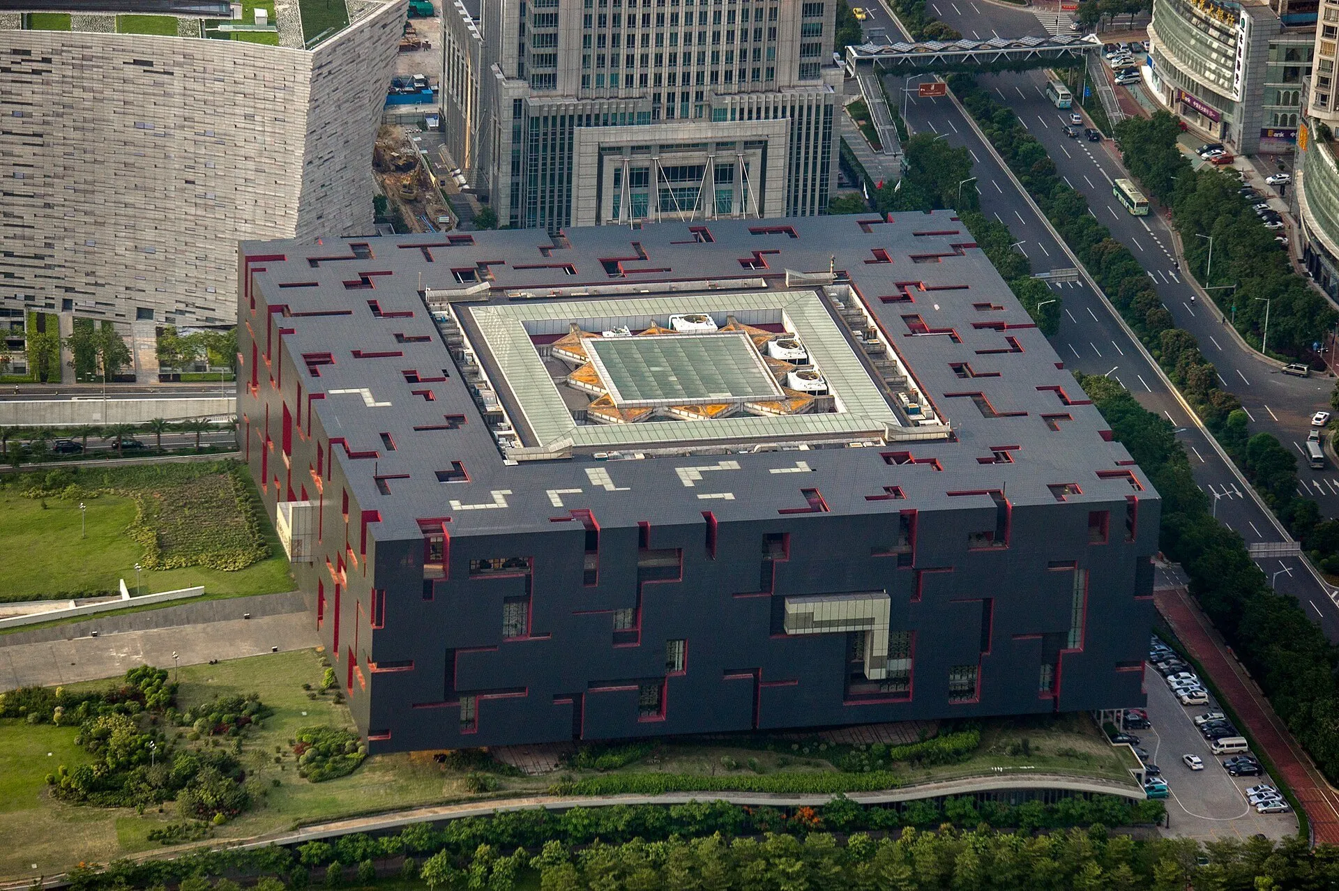 Vista elevada do Museu de Guangdong, com fachada cinza, recortes vermelhos, pátio central e ruas ao redor.