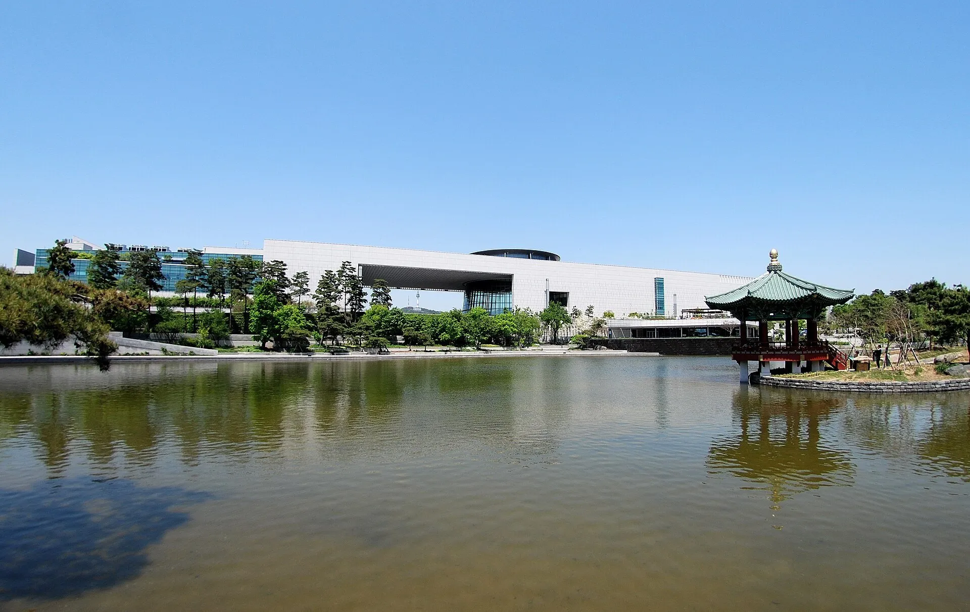 Museu Nacional da Coreia junto a um lago, com abertura central no edifício e pavilhão à direita.