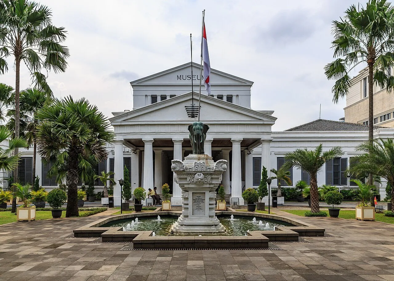 Fachada do Museu Nacional da Indonésia com estátua de elefante, fonte e palmeiras.