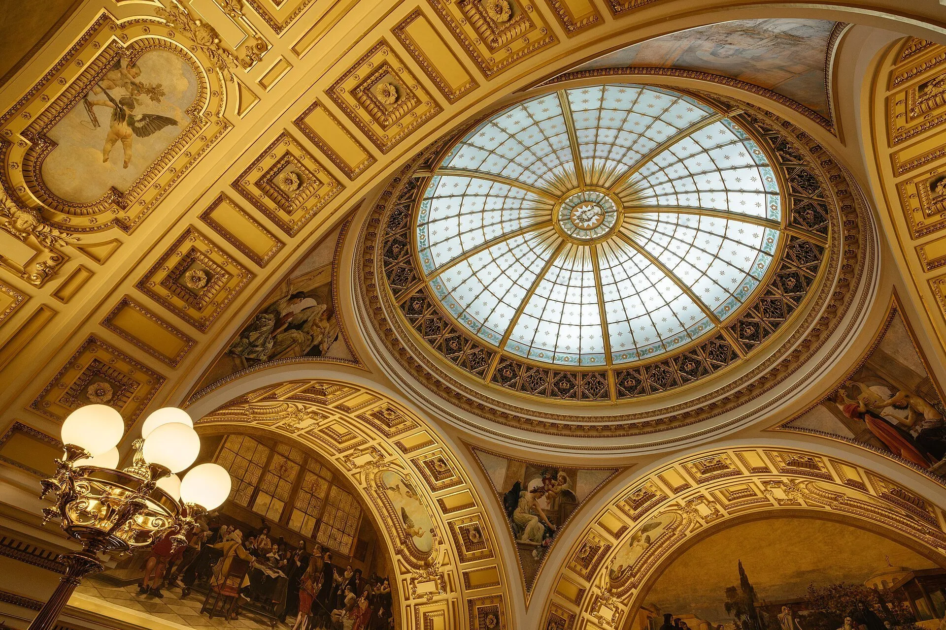 Cúpula envidraçada do Museu Nacional de Praga, cercada por pinturas, ornamentos dourados e um lustre.