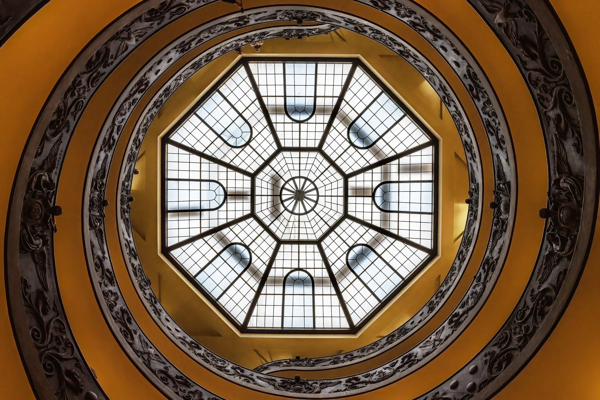 Escada em espiral dos Museus Vaticanos vista de baixo, com a claraboia octogonal no centro e corrimão ornamentado.