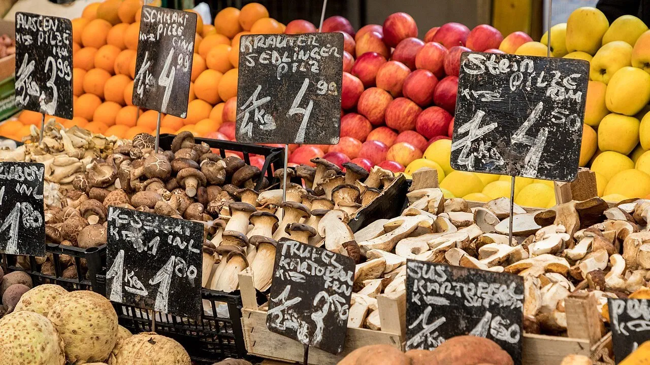 Banca do Naschmarkt com cogumelos, maçãs, peras, laranjas e pequenas placas de preços em alemão.