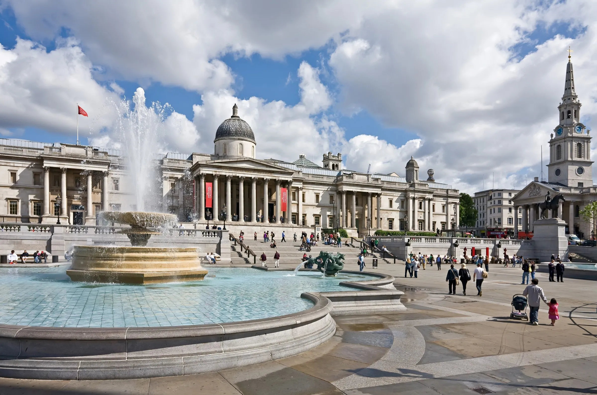 Fachada de colunas da National Gallery vista da Trafalgar Square, com a fonte em primeiro plano e a igreja ao fundo.