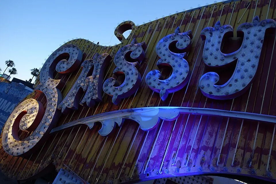 Letras antigas do letreiro Sassy Sally’s no Neon Boneyard, com iluminação azul e céu ainda claro.