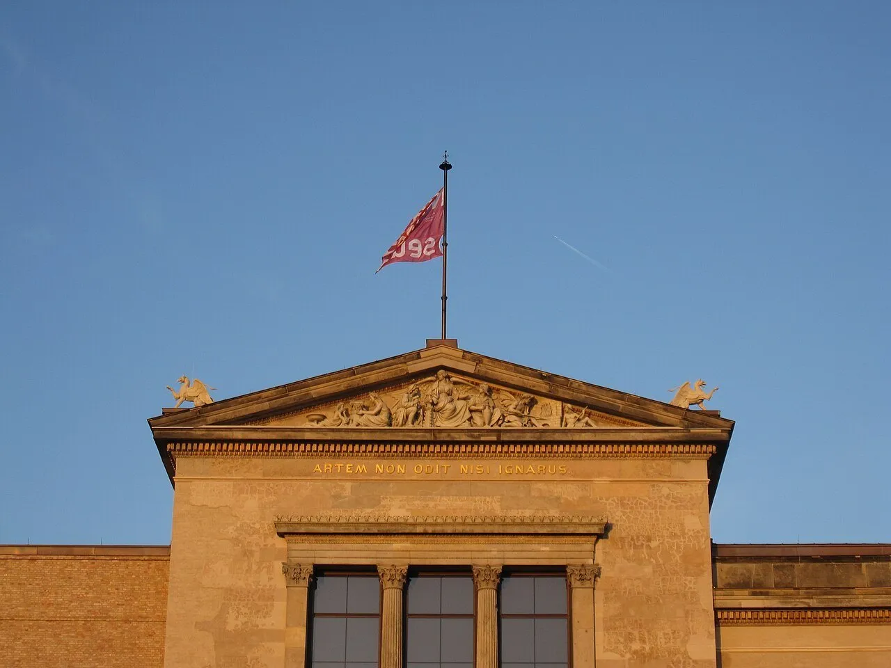 Detalhe superior da fachada do Neues Museum, com frontão esculpido, bandeira e janelas.