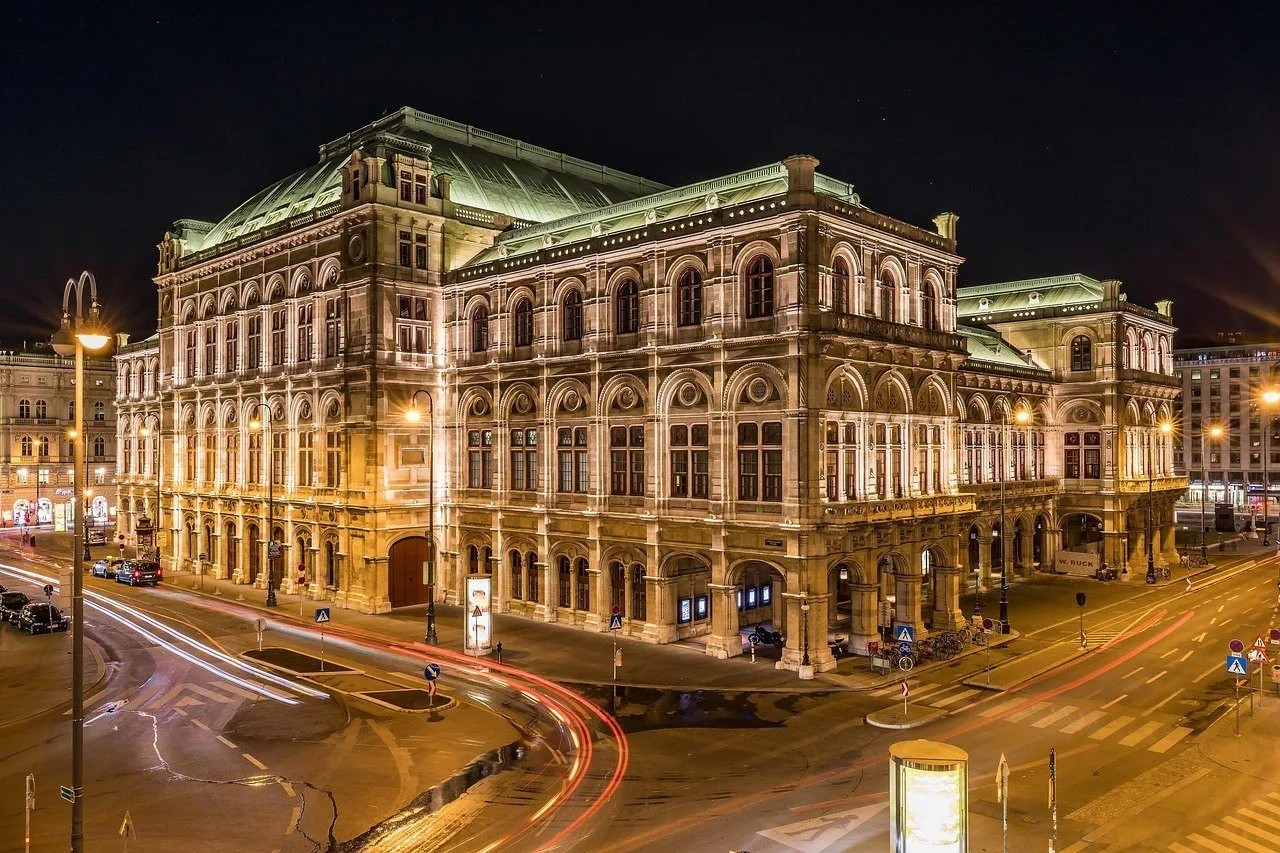 Ópera Estatal de Viena iluminada à noite, com rastros de luz dos veículos nas ruas ao redor.