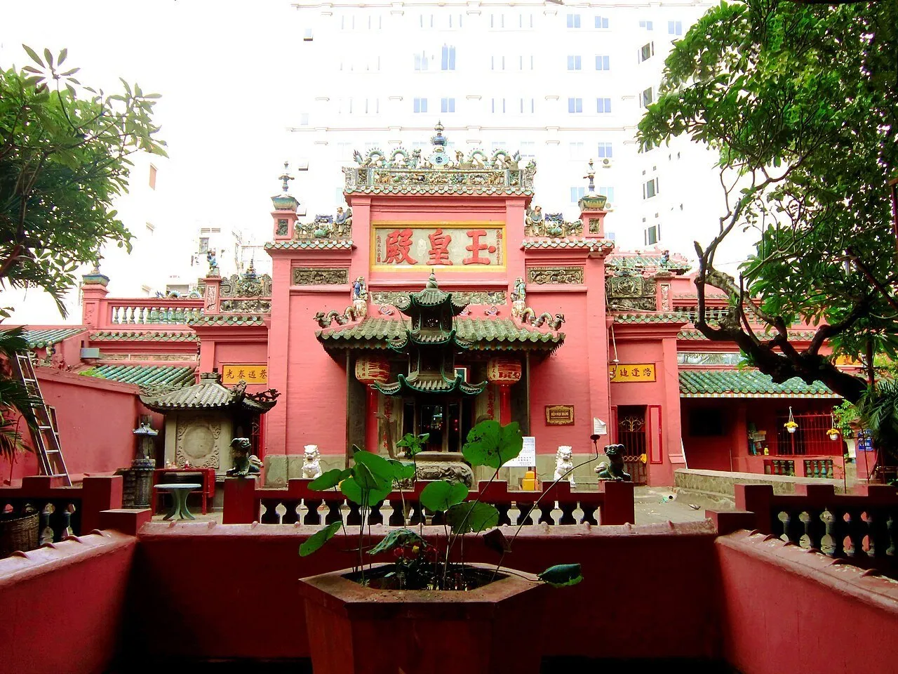 Fachada vermelha do Pagode do Imperador de Jade, com telhados verdes, árvores e incensário no pátio.