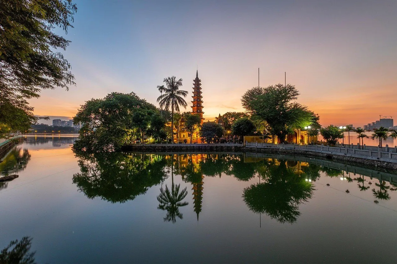 Pagode Tran Quoc ao entardecer, com torre de tijolos, árvores e reflexos na água.