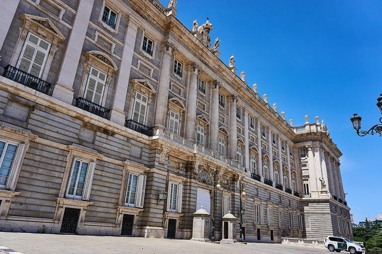Fachada de pedra do Palácio Real de Madri em perspectiva, com janelas, estátuas e céu azul.