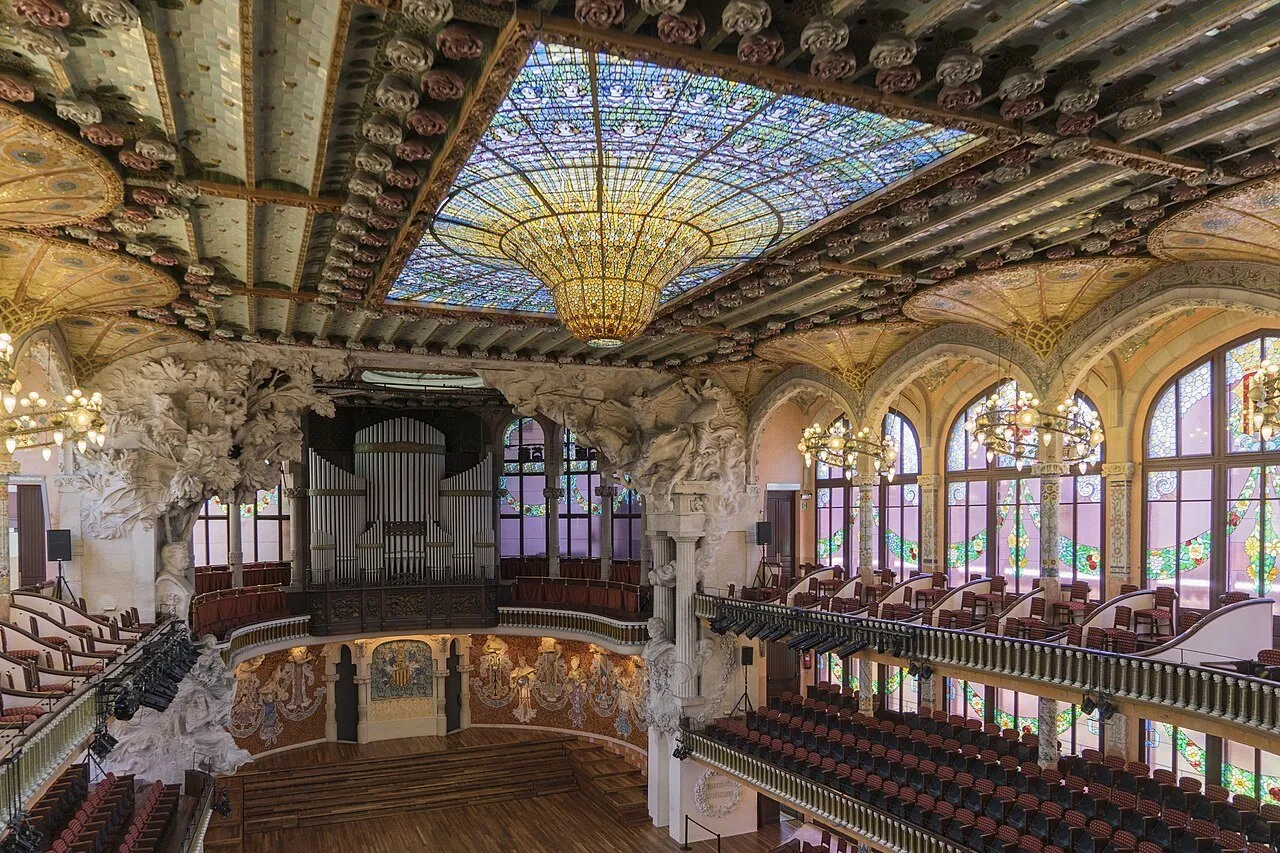 Sala de concertos do Palau de la Música Catalana com claraboia de vitrais, órgão e balcões.