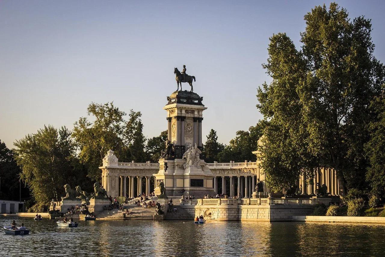 Monumento a Alfonso XII junto ao Estanque Grande do Retiro, com barcos e árvores em luz dourada.