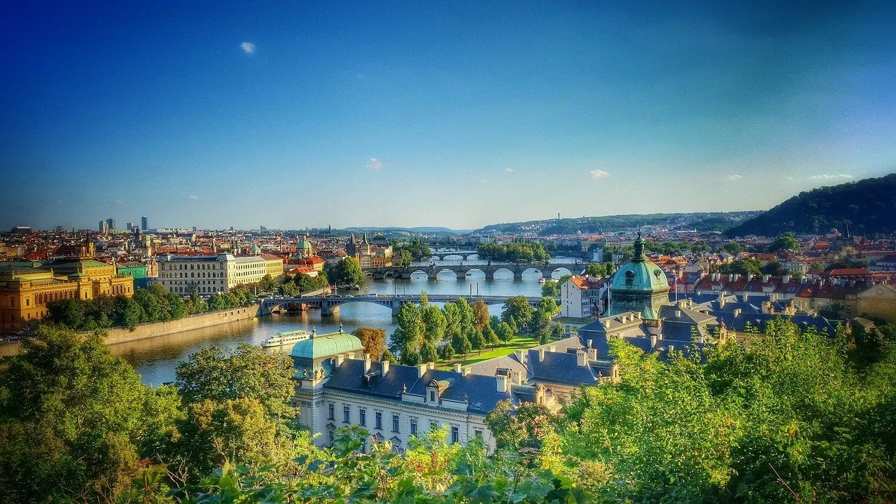 Vista de Letná com árvores em primeiro plano, telhados e uma sequência de pontes sobre o Vltava.