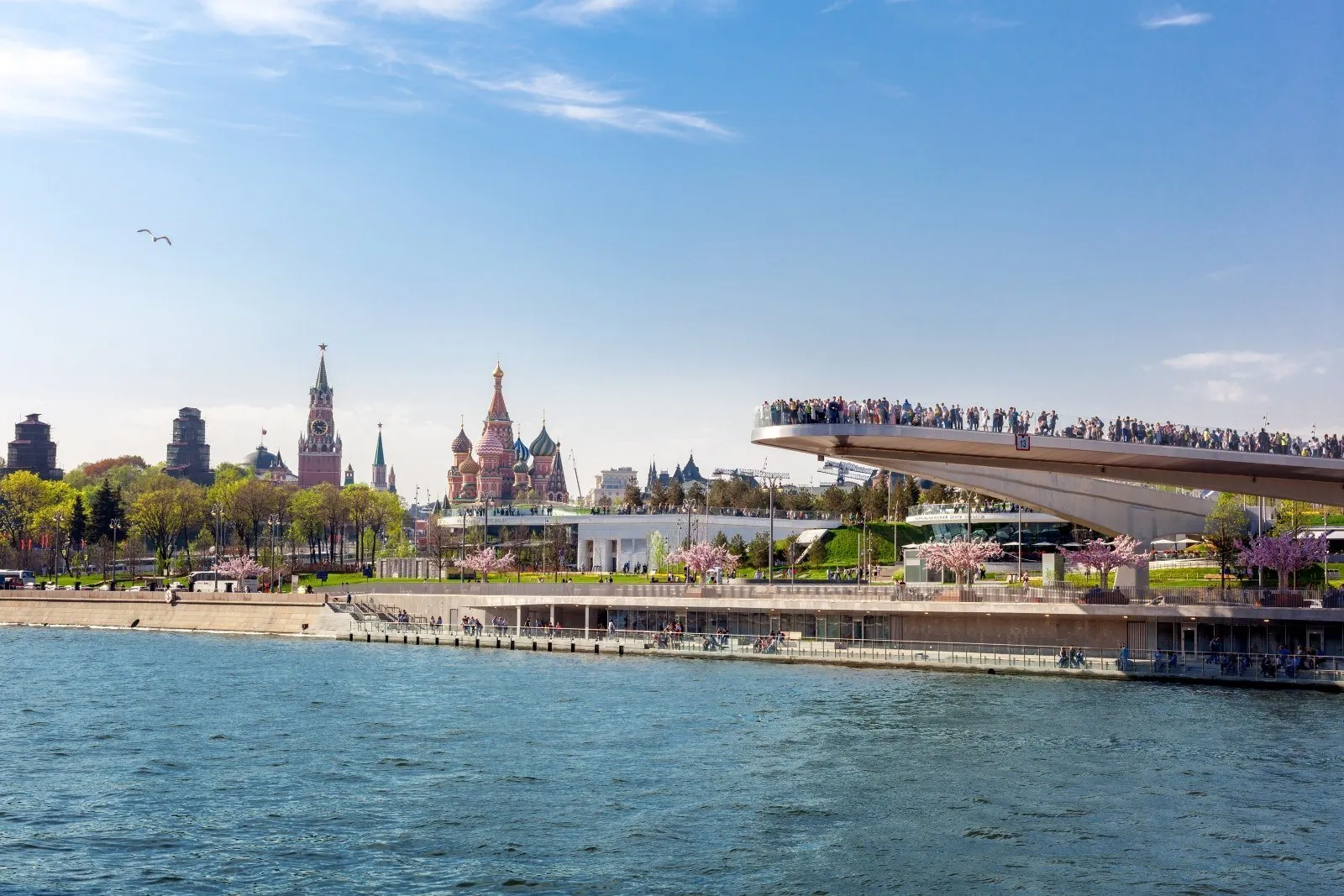 Ponte-mirante do Zaryadye sobre o rio Moscova, com parque, árvores floridas e São Basílio ao fundo.