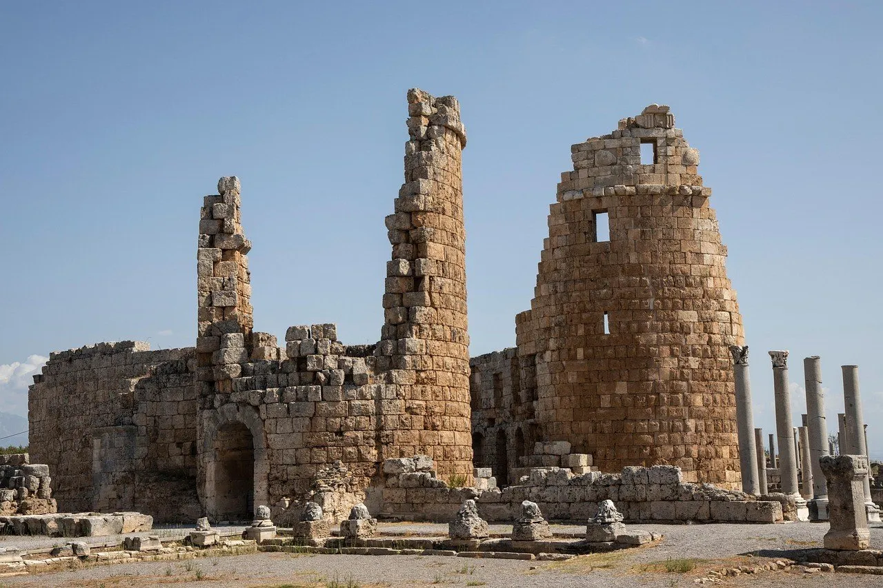 Ruínas das duas torres do portão helenístico de Perge, em pedra clara, com colunas à direita e céu azul sem nuvens.