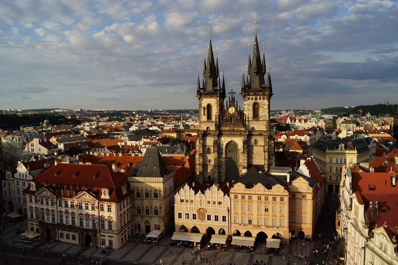 Torres da Igreja de Týn sobre a Praça da Cidade Velha, cercadas por telhados vermelhos e fachadas claras.