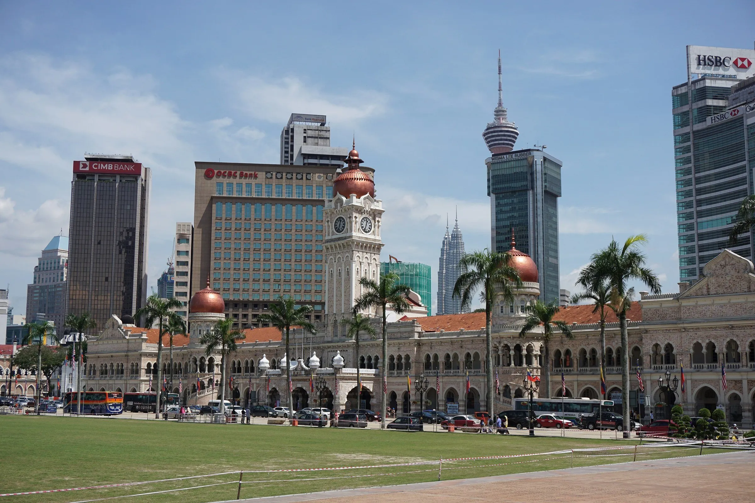 Edifício Sultan Abdul Samad, com arcos e torre do relógio, visto do gramado da Praça Merdeka, com arranha-céus atrás.