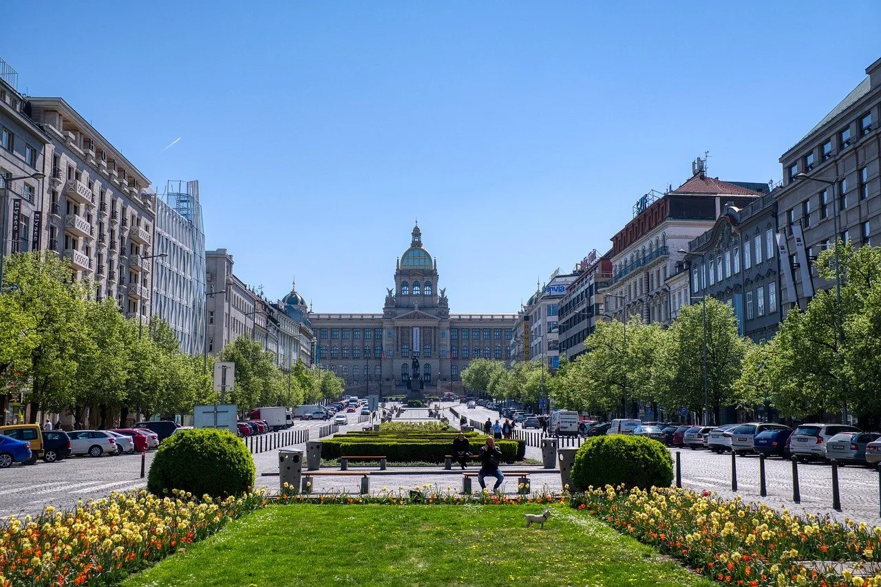 Praça Venceslau com jardins, pedestres, estátua equestre e fachada do Museu Nacional ao fundo.