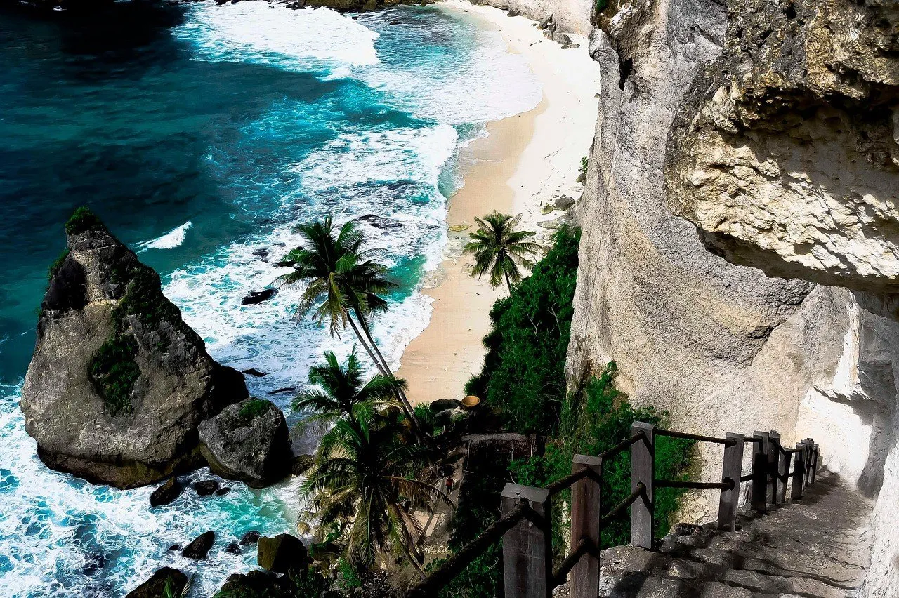 Escada na falésia de Diamond Beach, com coqueiros, rochedo pontudo, areia clara e ondas azuis em Nusa Penida.