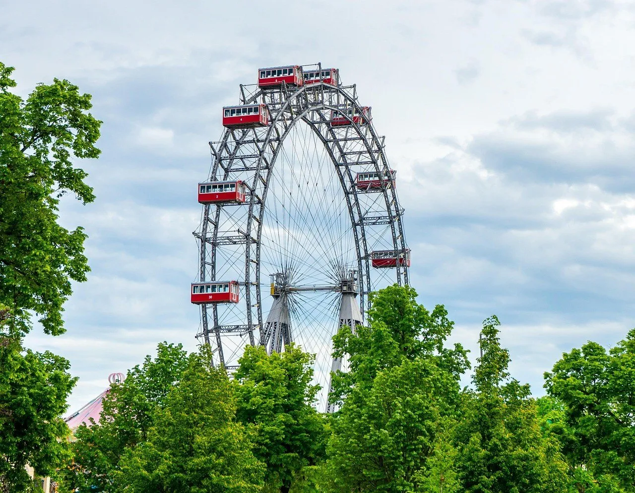 Roda-gigante histórica do Prater com cabines vermelhas, parcialmente cercada por árvores verdes.