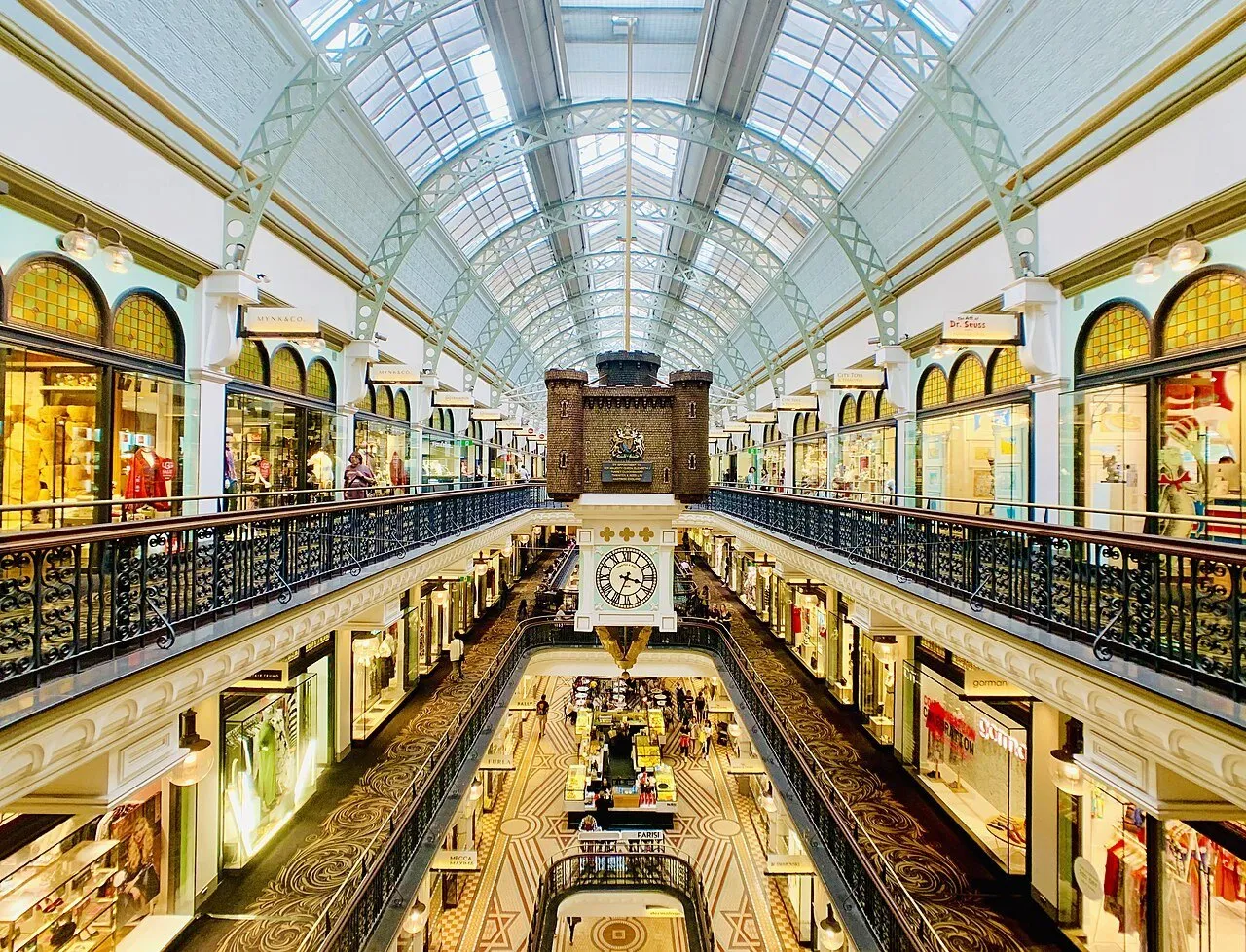 Galerias internas do Queen Victoria Building, com relógio suspenso, balaustradas e cobertura de vidro.