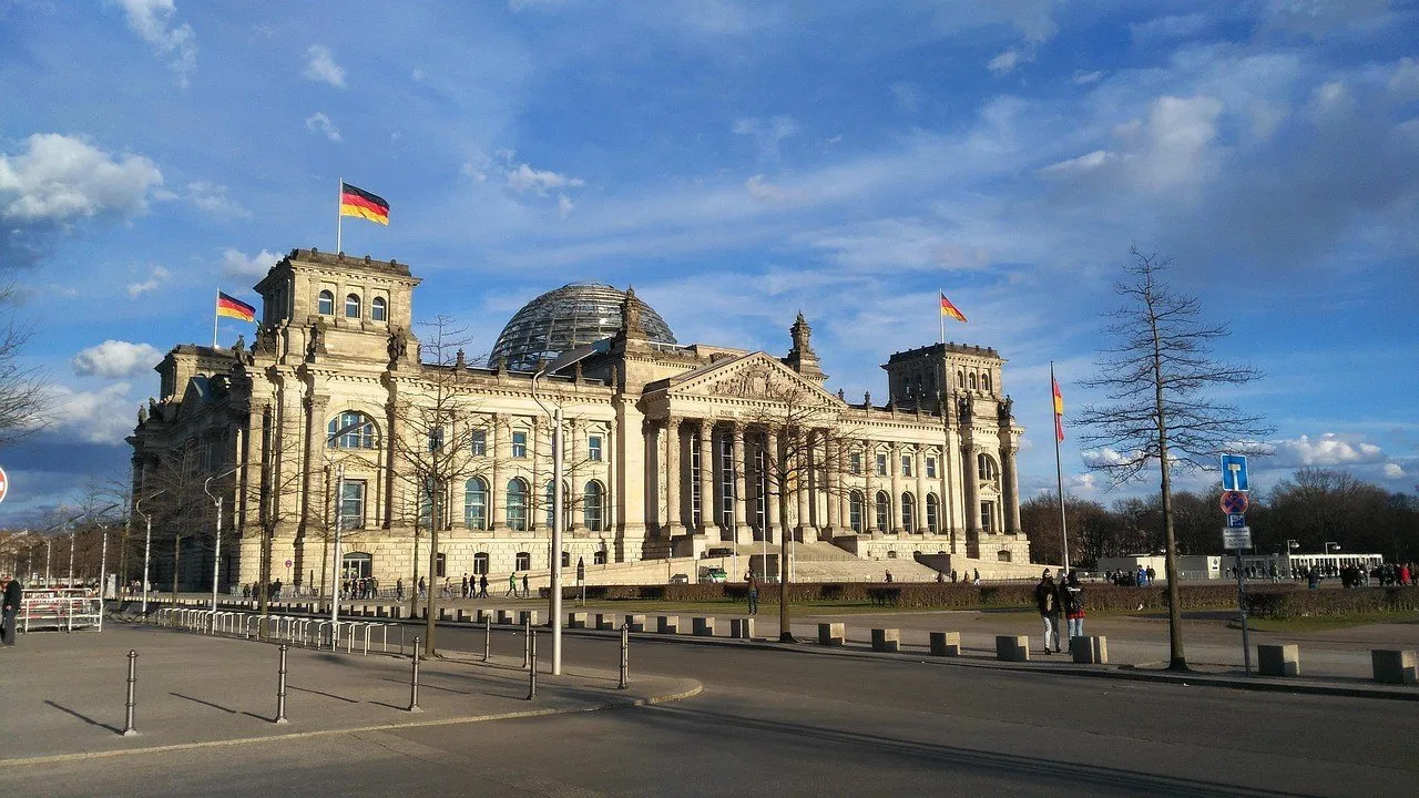 Fachada externa do Reichstag com cúpula de vidro e bandeiras alemãs sob céu azul.