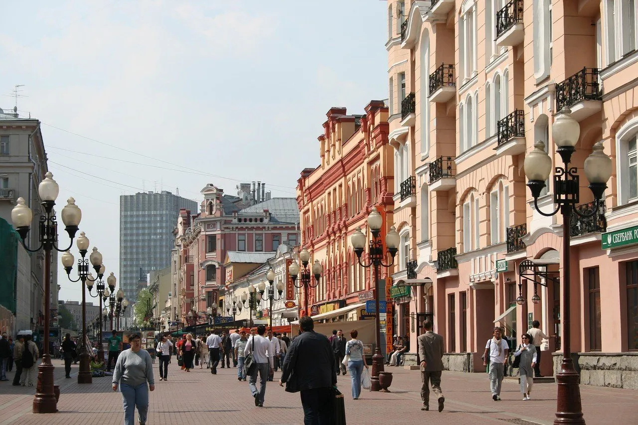 Rua Arbat de pedestres, em Moscou, com fachadas coloridas, postes e pessoas caminhando.