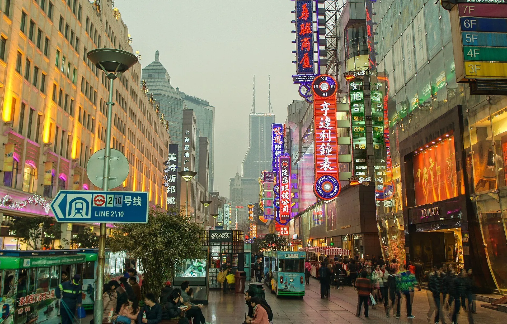 Rua Nanjing Leste com letreiros iluminados, fachadas comerciais, veículos turísticos e pedestres.