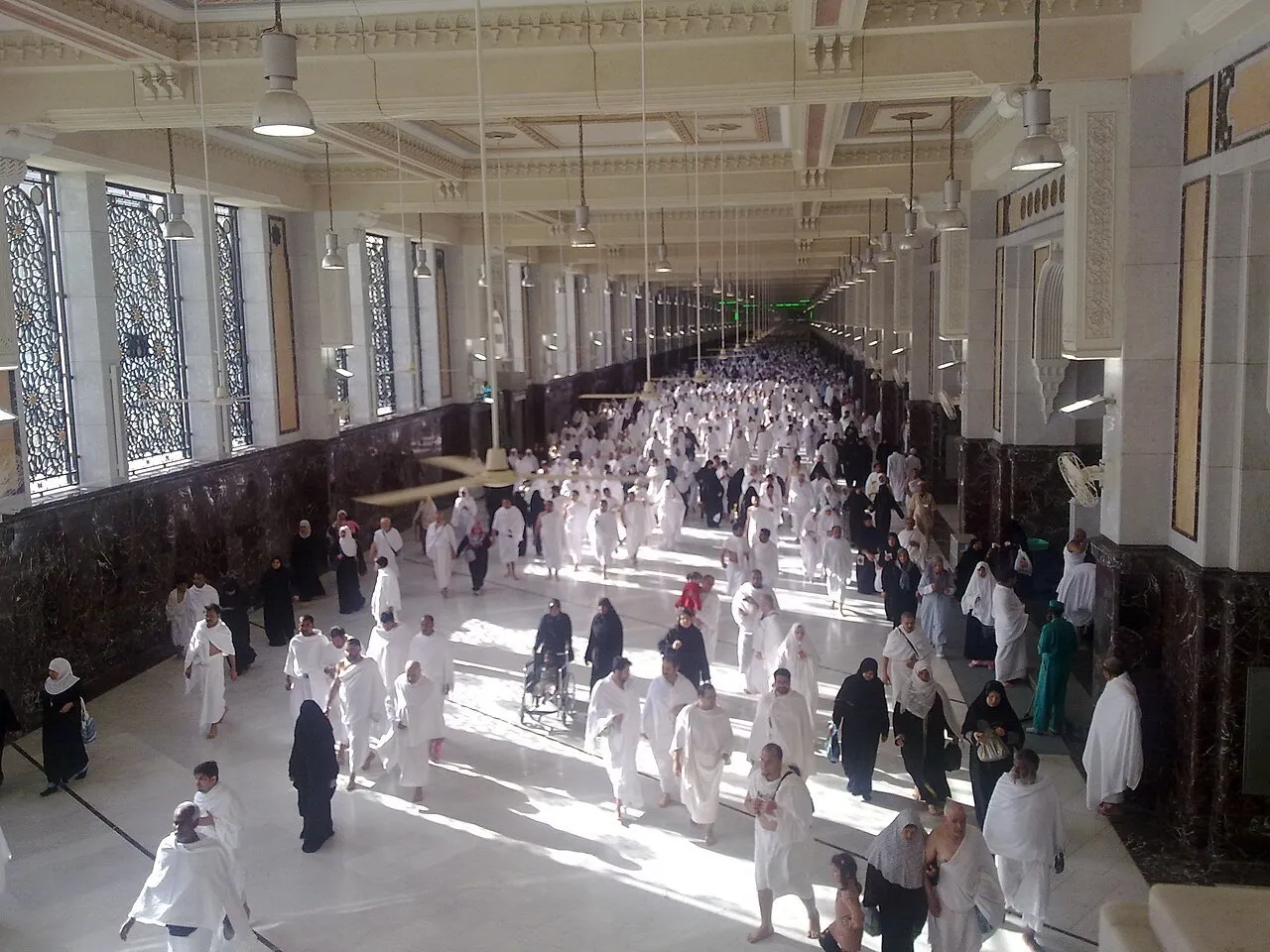 Galeria do mas’a entre Safa e Marwa, com janelas trabalhadas, colunas e peregrinos caminhando.