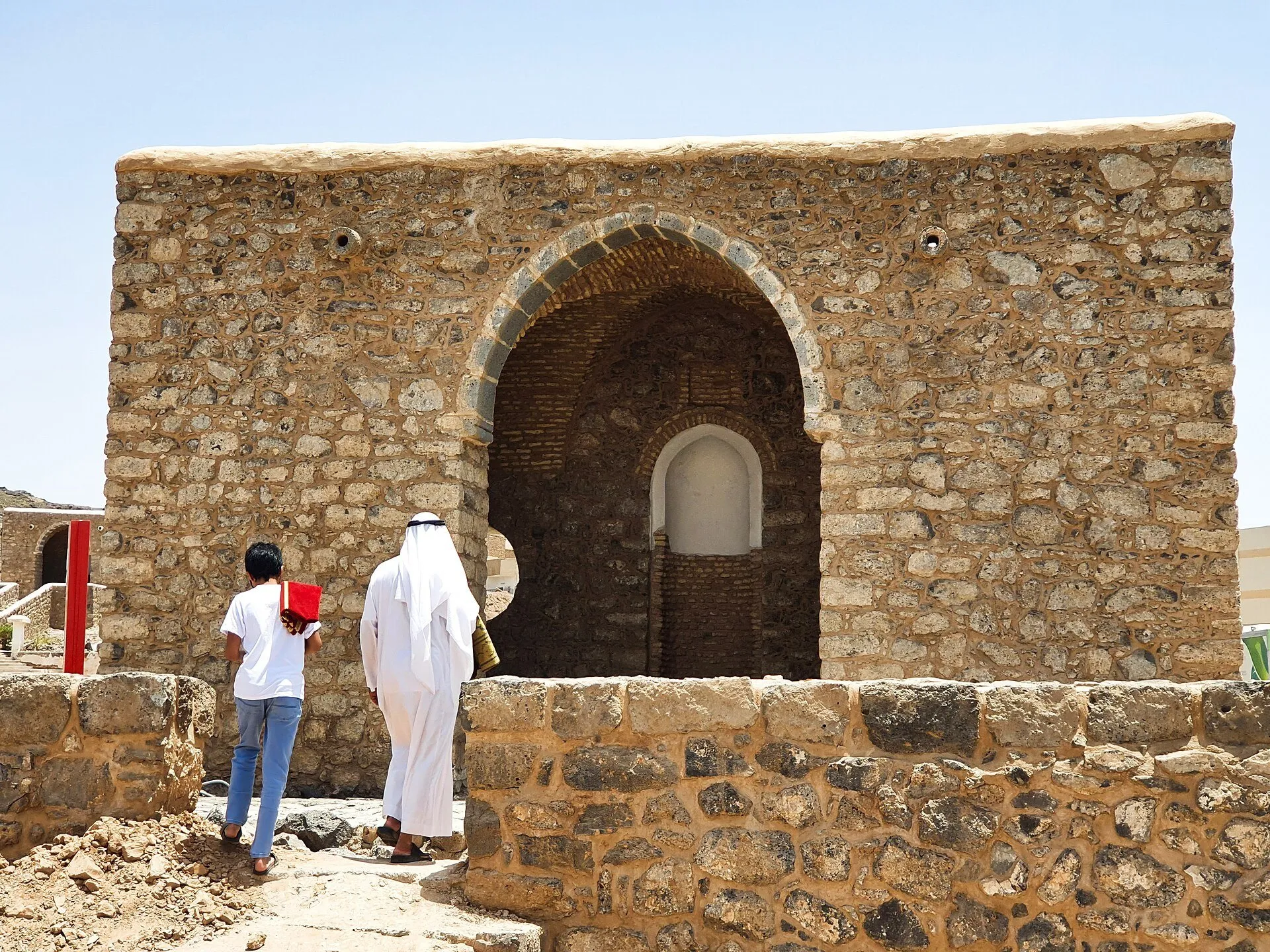 Parede e nicho em arco da mesquita de Umar ibn al-Khattab, com dois visitantes de costas.