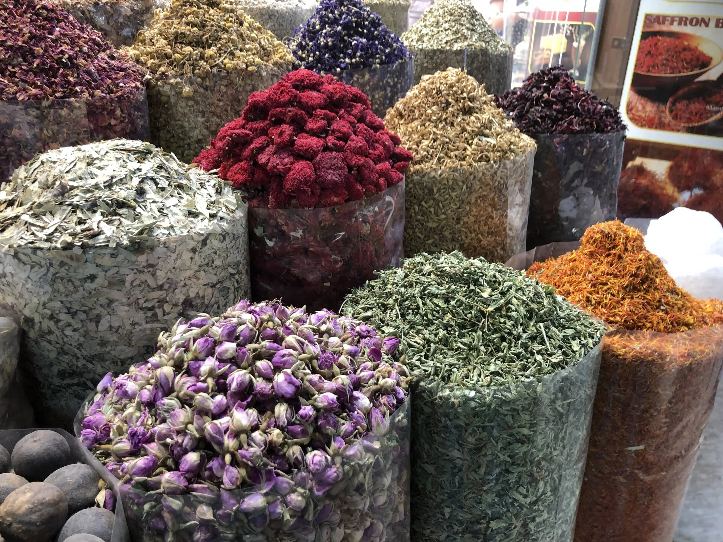 Sacos abertos de especiarias, flores secas e ervas em tons de roxo, vermelho, verde e laranja numa loja do souk de Deira.