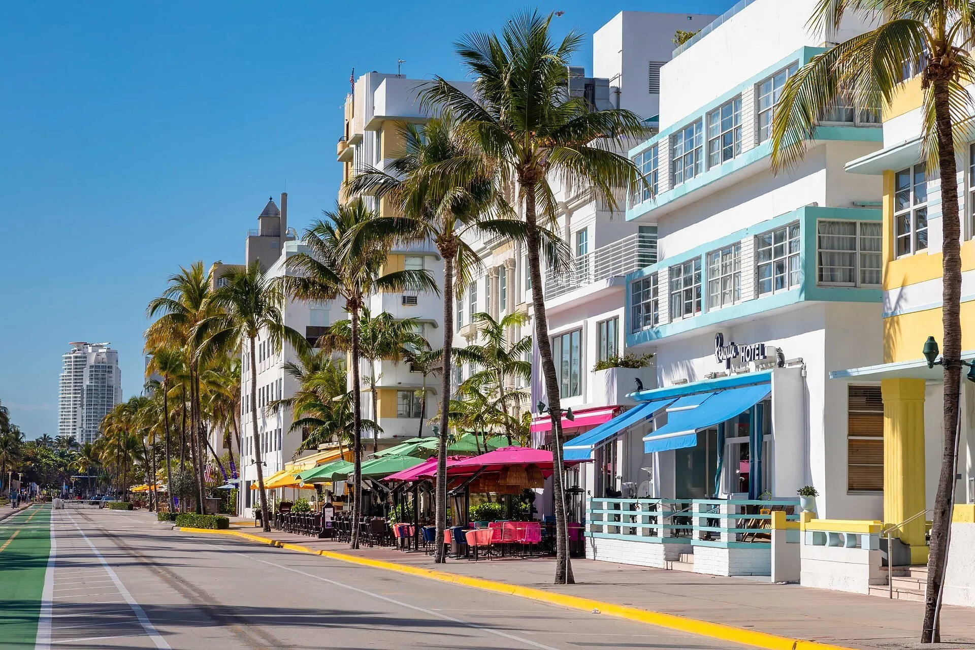 Fachadas claras e coloridas de hotéis Art Déco em Ocean Drive, com palmeiras e faixa de bicicletas.