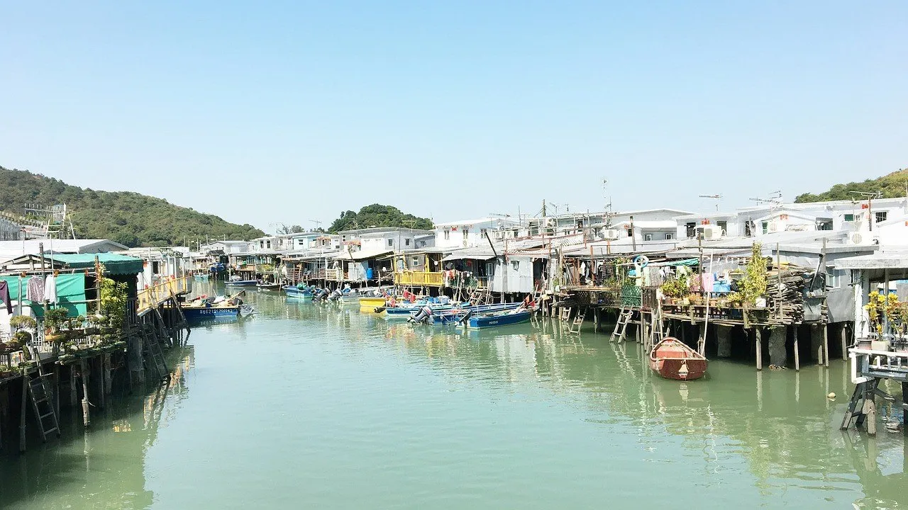 Canal de Tai O, em Lantau, com casas de palafita, barcos de pesca atracados e colinas verdes ao fundo.