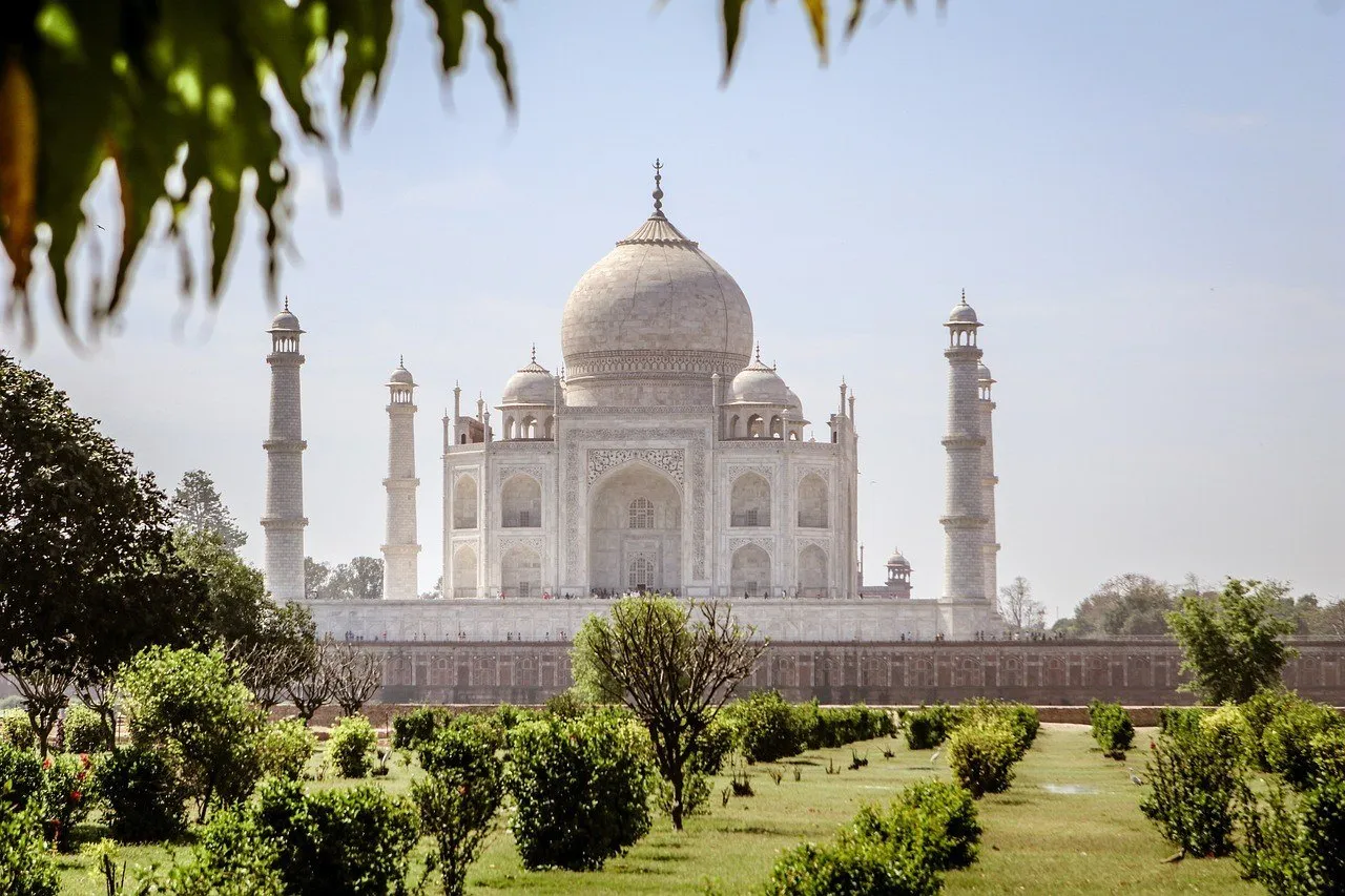 Taj Mahal visto de lado no jardim, com arbustos e folhas em primeiro plano.