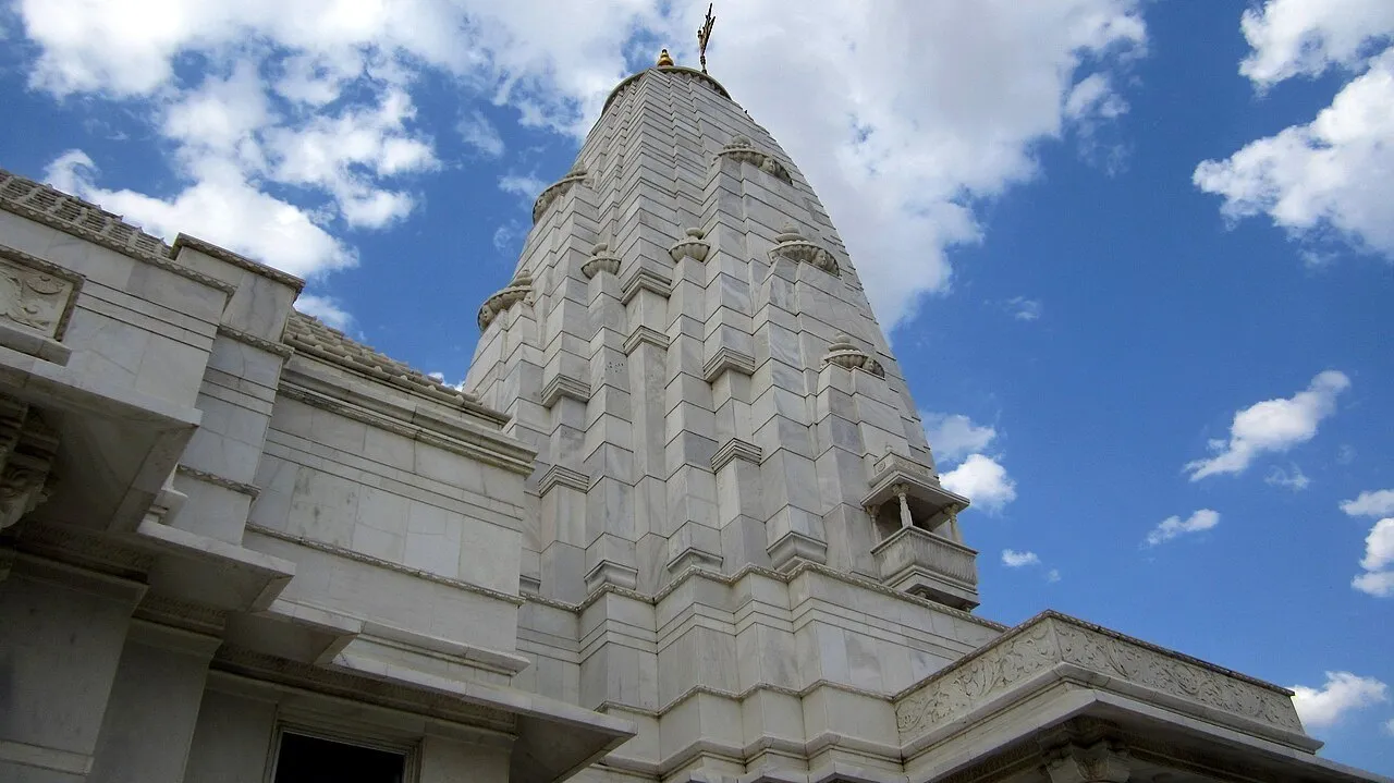 Torre de mármore branco do Templo Birla de Jaipur, vista de baixo sob céu azul com nuvens.