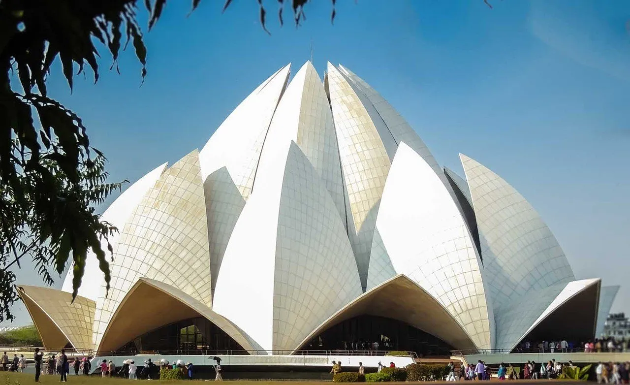 Templo de Lótus, em Nova Délhi, com pétalas de mármore branco contra céu azul e visitantes pequenos ao pé.
