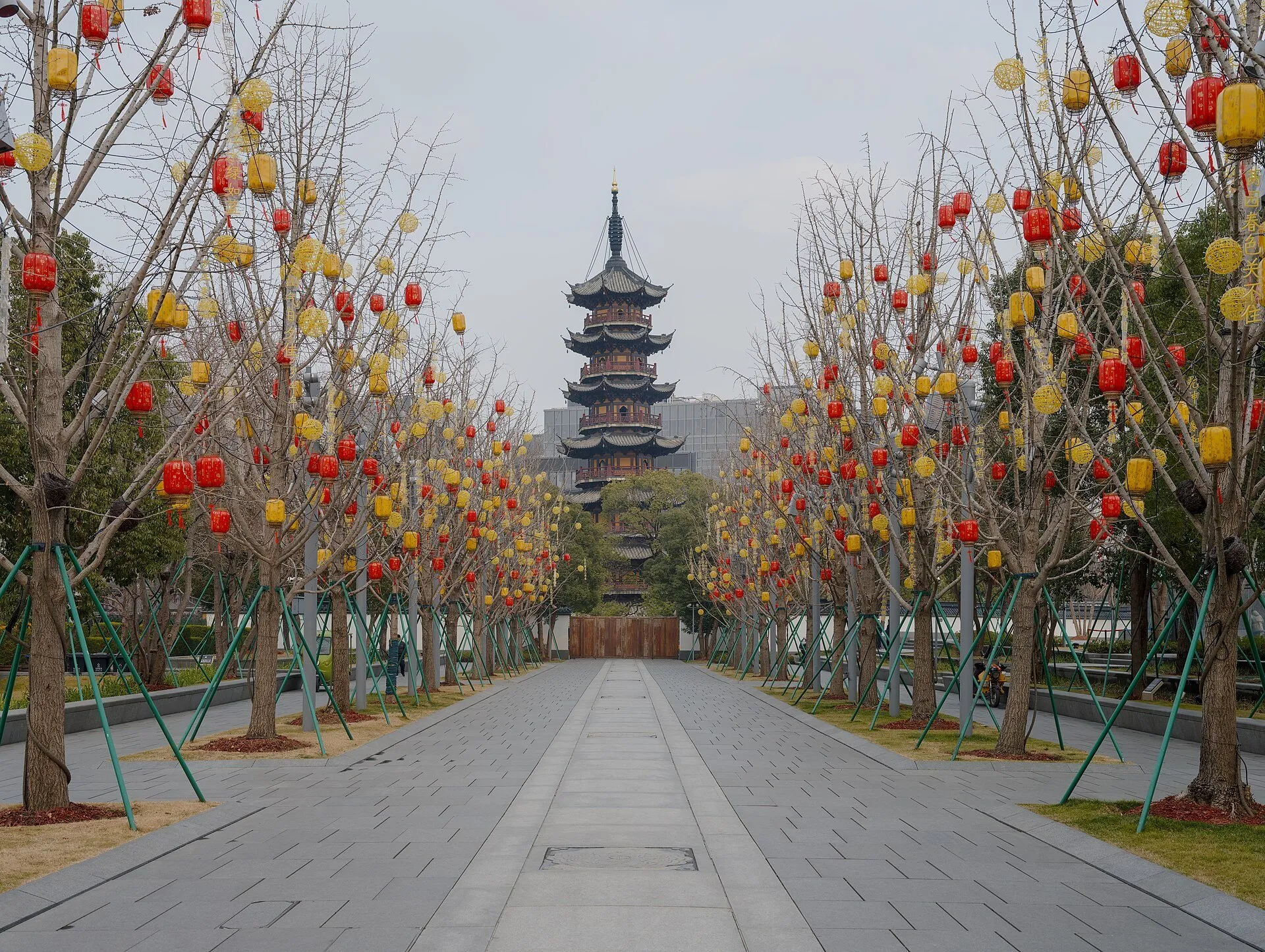 Pagoda de Longhua ao fundo de uma alameda com árvores e lanternas vermelhas e amarelas.