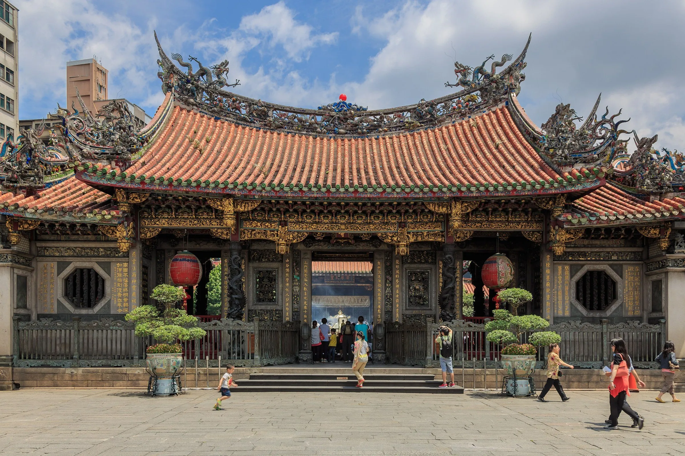 Entrada do Templo Longshan, com telhado ornamentado, lanternas e visitantes no pátio.