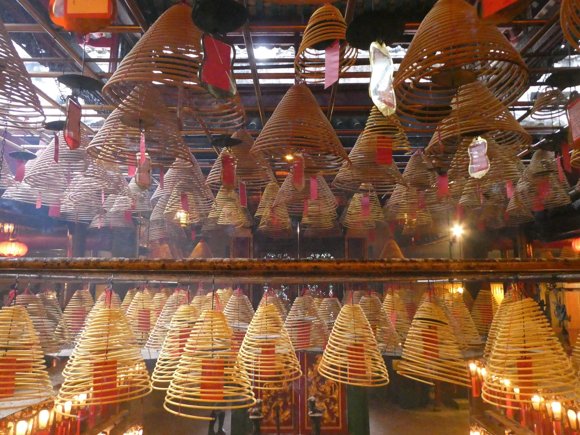 Espirais de incenso penduradas no teto do Templo Man Mo, com etiquetas vermelhas e luz quente entrando pelo alto.