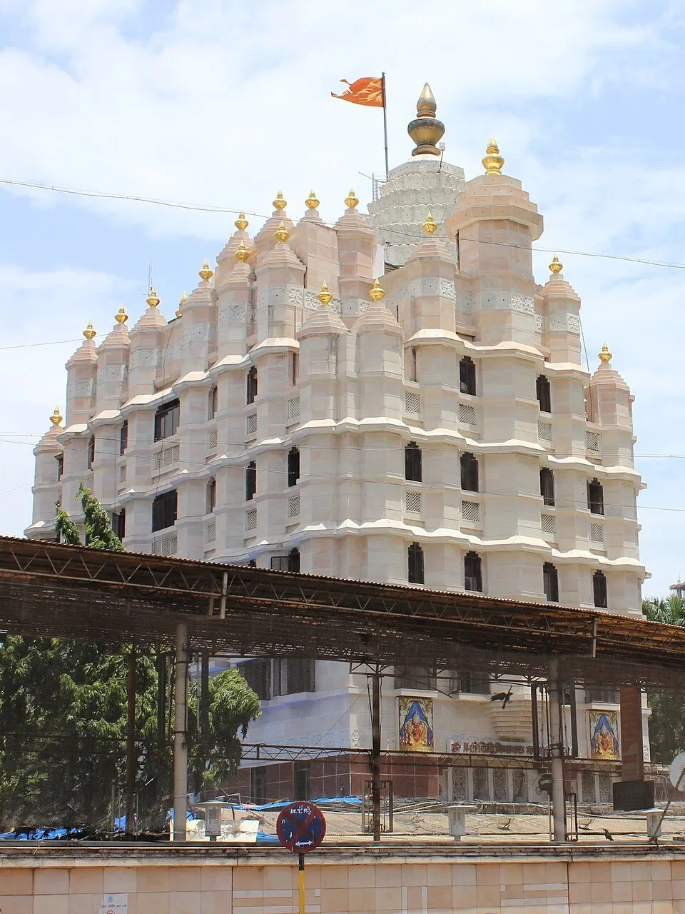 Fachada clara do Templo Siddhivinayak, em Mumbai, com torres escalonadas, remates dourados e bandeira.