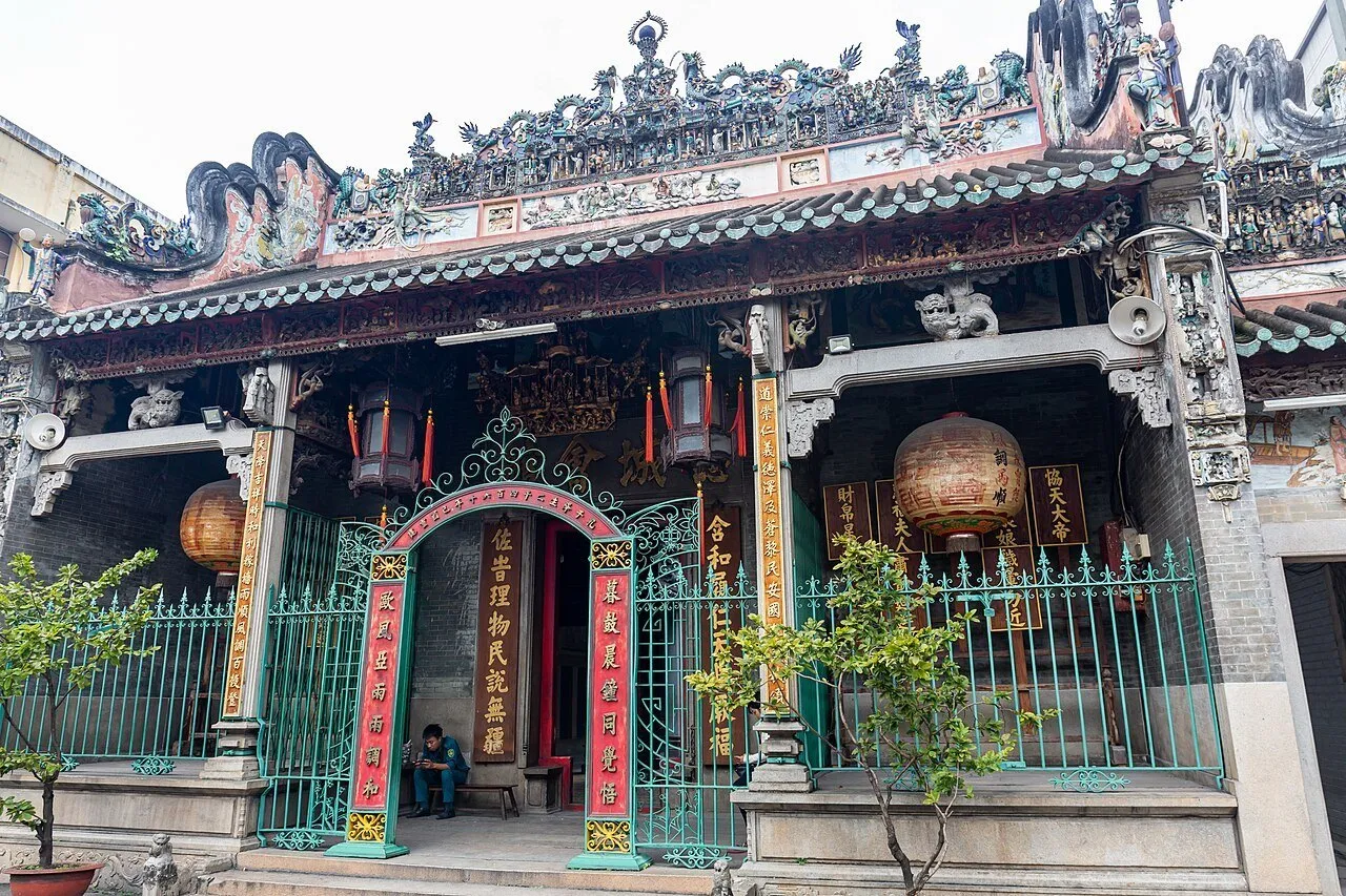 Fachada do Templo Thiên Hậu de Chợ Lớn com portão verde, lanternas e figuras de cerâmica no telhado.