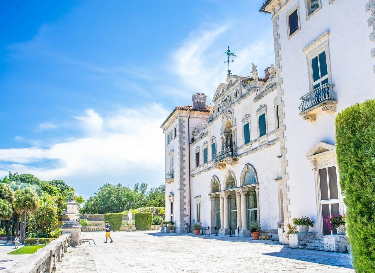 Fachada clara de Vizcaya, em Miami, vista de lado com arcos, terraço de pedra e vegetação ao redor.