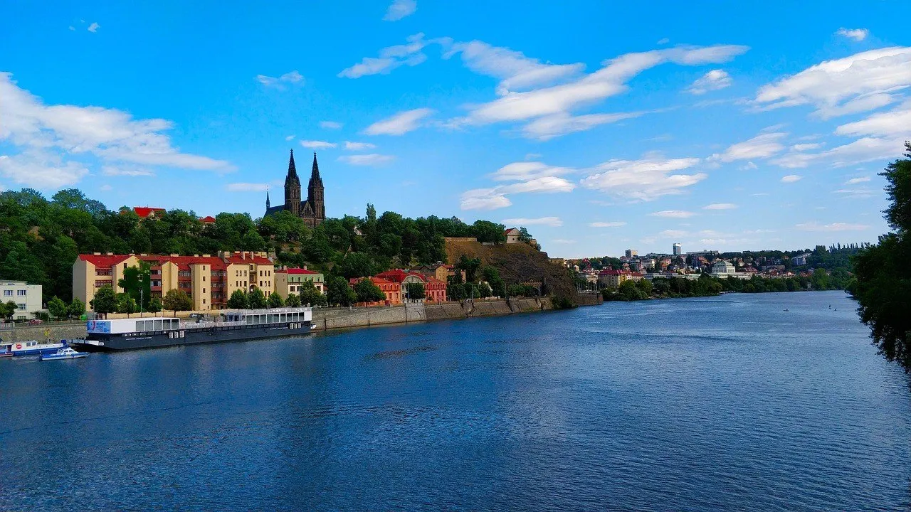 Vyšehrad visto do Vltava, com muralhas, árvores e as duas torres da Basílica de São Pedro e São Paulo.