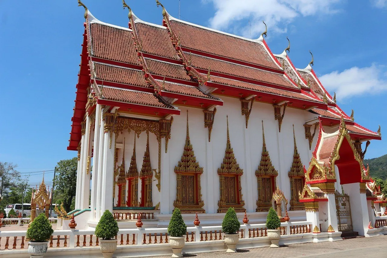 Salão principal do templo Wat Chalong, em Phuket, com paredes brancas, telhado vermelho escalonado e céu azul ao fundo.