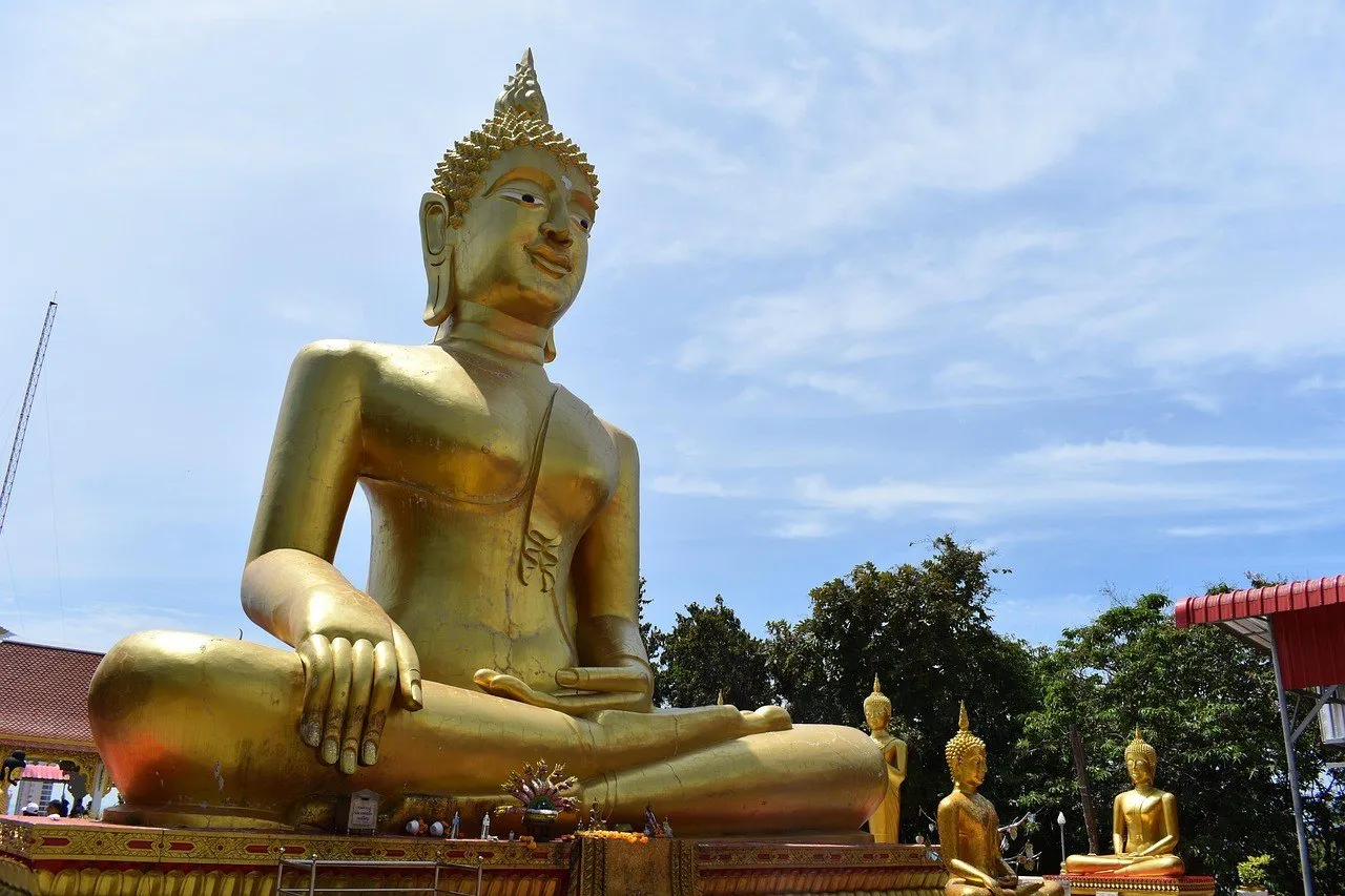 Buda dourado sentado do Wat Phra Yai, em Pattaya, visto de baixo sob céu azul.